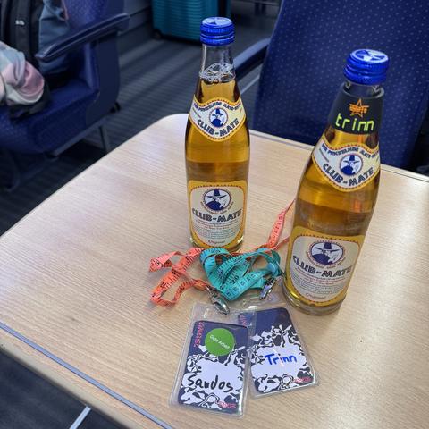 Zwei Flaschen Clubmate und zwei Engelbadges vom 38c3 auf einem Tisch im ICE.