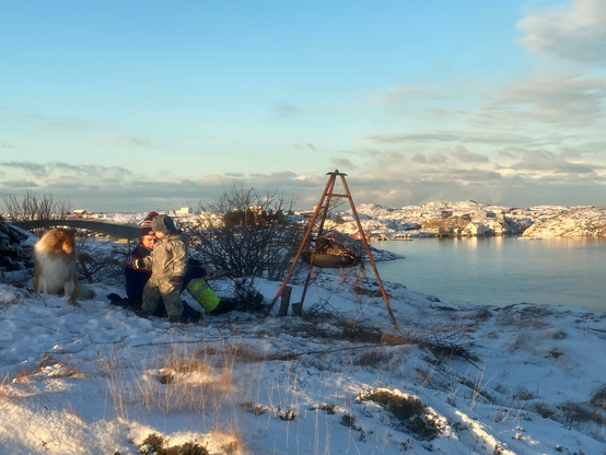 Color image of coastal Norway, Mausund, Trondelag. Father and son enjoy a fire lit for the New Year above the harbor, overlooking the North Atlantic's Norwegian Sea. Image shows the sun rising opposite the fire, its tripod holding the burning embers aloft, while the Sons of Odin - or just a father and his toddler son - enjoy the view across the harbor.