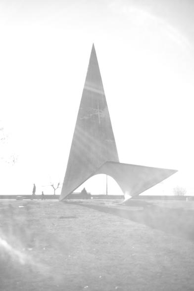 A giant statue on a field with people passing by.