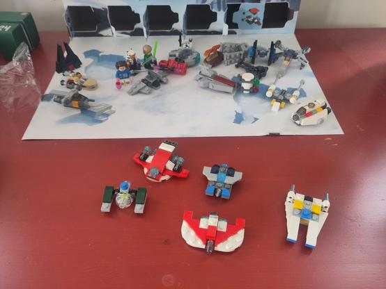 The contents of a Lego Star Wars advent calendar. All doors are opened and the models built. There are figures like Luke Skywalker and ships like the X-Wing fighter, but also models from newer shows and movies.
