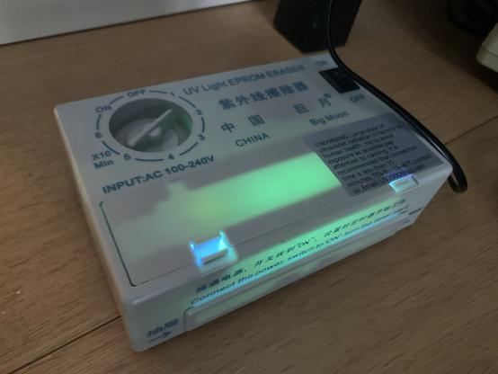 A cheap looking Chinese UV Eraser for EPROMs is glowing eerily in green.