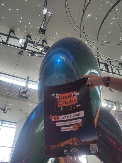 Das Plakat des InselChaos 2025 vor der großen fairydust Rakete im Foyer des #38c3
