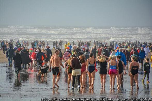 View of a English beach, a cold sea with rollers beyond. A large number of people are walking towards the sea for the new year swim.