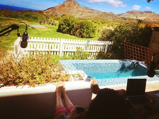 Photo of a pool with blue sky and mountain in the background and feet in the foreground and a microphone on the left