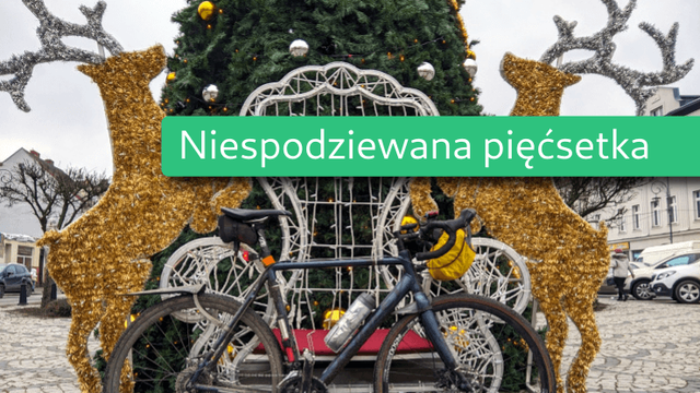 Miniaturka dla wpisu „Grudzień na rowerze”. Na zdjęcie roweru szutrowego opartego o świąteczną dekorację nałożony zielony pasek z napisem „Niespodziewana pięćsetka”.