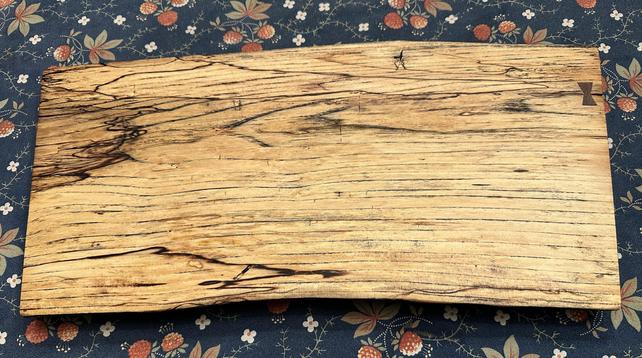 A wooden board with a natural, wavy edge and distinct grain patterns, resting on a floral-patterned fabric background.