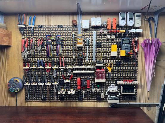 A wooden wall covered with a ridged 3D printed black mesh of connection points. A variety of small tools hang from custom printed holders. Pliers, vice grips, wire cutters dominate the left side of the board. Screwdrivers, hex bits, drill bits are in the lower center. The upper right is all 120V things, adapters, unused smart home plugs and usage meters. The lower right has lithium batteries and their charger.  My grandmother's parasol from the 1930s hangs to the right of the board.

In the middle at the top is my bottle of ibuprofen.