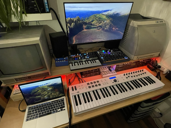 A quite busy bench with a few synthesisers, a master keyboard and two computers (one of which is a vintage C128D)