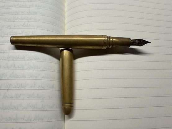 SKB fountain pen meds out of bronze laying across open Fabriano lined notebook. Pen is uncapped and the cap lays along the seaming the notebook