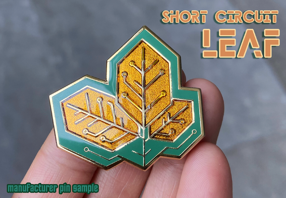 Photo of a hand holding up a hybrid enamel pin of leaves designed to look like a printed circuit board (PCB). Text on the image reads: "Short Circuit", "Leaf", and "manufacturer pin sample".