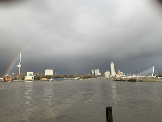 Panoramic view of Rotterdam, seen from the south side of the river with dark clouds and a rainbow in the distance. Left to right: rainbow, Euromast, entry building of the Maastunnel, Erasmus Medical Centre, Het Park, Zalmhaven (highest tower in the country), Erasmusbrug.