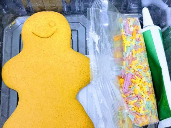 A gingerbread figure in a clear plastic tray. The section on the right contains a green tube of icing and two packets of sugar decorations.