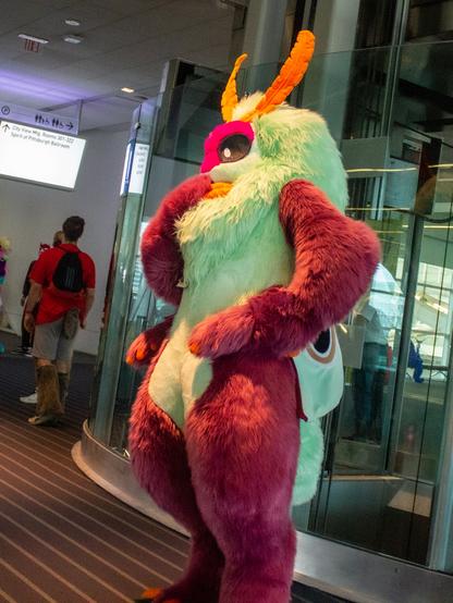 A large moth fursuit holding their hand over their mouth viewed from the side.
