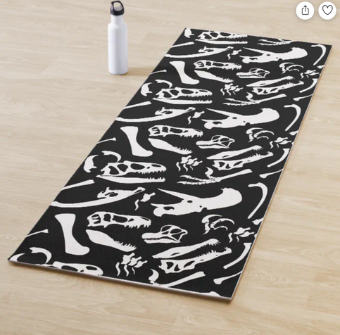 Photo of a yoga mat with a black and white pattern of various dinosaur bones. Dinosaur species include T-Rex, Allosaurus, Parasaurolophus, Brachiosaurus, Spinosaurus, and Triceratops.