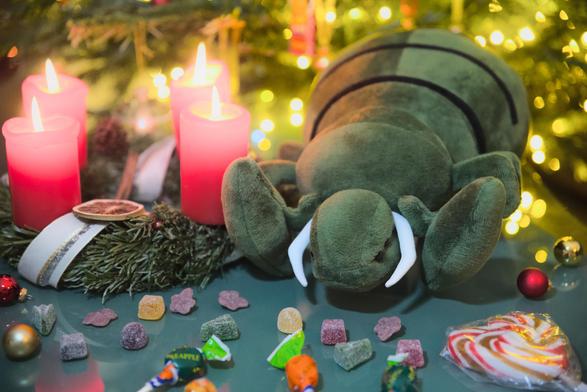 A plushy granger sits with some candies next to a Christmas tree and and fully lit Advent wreath.