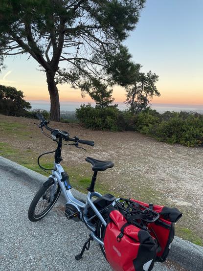 Pale pink-orange colors of sunset above the Monterey Bay. A Tern NBD bicycle with red panniers is parked along the edge of the road.