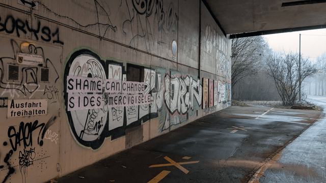 The photo shows the wall of an underpass on the left side with graffitis and a feminist collage that reads: «SHAME CAN CHANGE SIDES - MERCI GISELE»