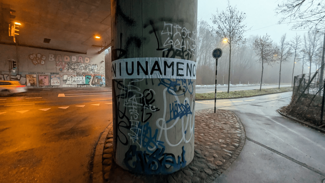 The photo shows a round pillar of an underpass with the street in the background. On the pillar is a feminist pasted collage  that reads: «#NIUNAMENOS»