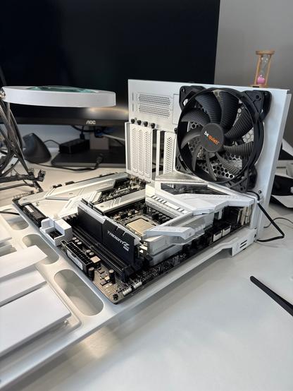 The "guts" of the computer, the L-shaped frame holding the motherboard and rear case fan, lays on my desk ready for maintenance work. There is one stick of RAM attached to the board. Still all black details with mostly white, except for the "be silent!" logo, which is white and orange. The black, 9-bladed, serrated, fan, is designed for extremely quiet operation (but not quiet enough for me - more on that another time). The case panels have well-designed hand-tightened screws (black) and the removable accessory panels are solid steel, painted white, and perforated with black holes for good airflow. It's all very spacey.