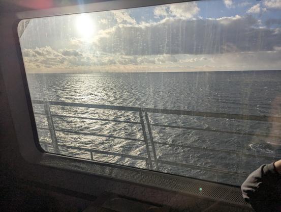 Blick aus Zugfenster auf Sonne mit Wolken über Meer, am Horizont Windräder