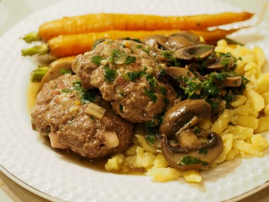 Zwei Salisbury Steaks (Frikadellen) mit einer leichten Pilzsauce auf Spätzle, daneben ein paar gegarte Karotten.