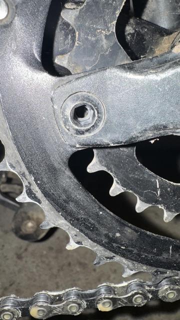 Eine Nahaufnahme eines Fahrradkettenrings und einer Kette, die die Zahnradzähne und ein Schraubenloch zeigt. Die Komponenten sind schmutzig, was auf die Verwendung hinweist.
