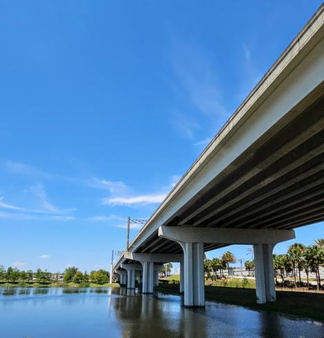 Upwards sloping on ramp for a bridge overpass stands partially in a pond, high up on strong columns.