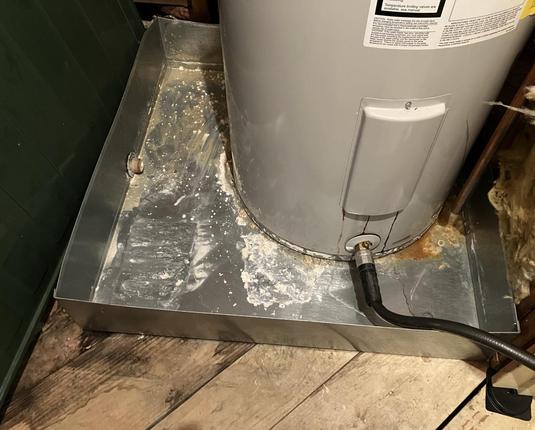 Water heater sits in a metal retention pan. A hose is hooked to the unit and running out of the attic.