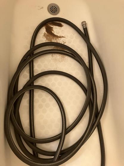 A black hose draining water and some nasty brown sludge out of my water heater into a bathtub.
