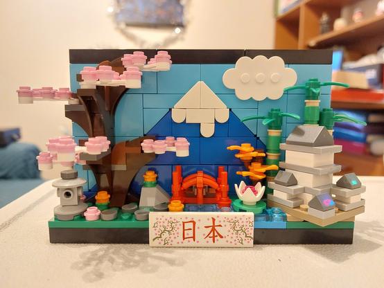 The Lego Japan Postcard. A small scene containing a cherry blossom tree, red bridge, bamboo plants, and Himeji castle, with Mount Fuji as the background.