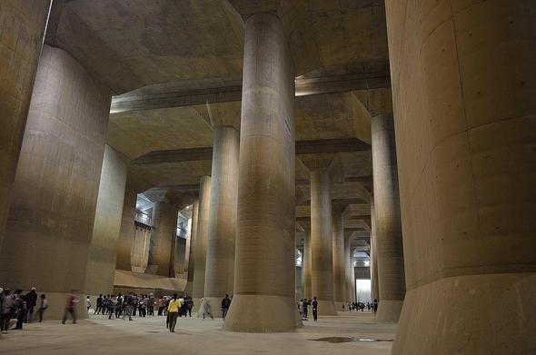 A picture of an underwater sewage / water retention system close to Tokyo. Massive grey columns and in proportion ant like humans can be seen. Looks like a cyberpunk cathedral or movie scene.