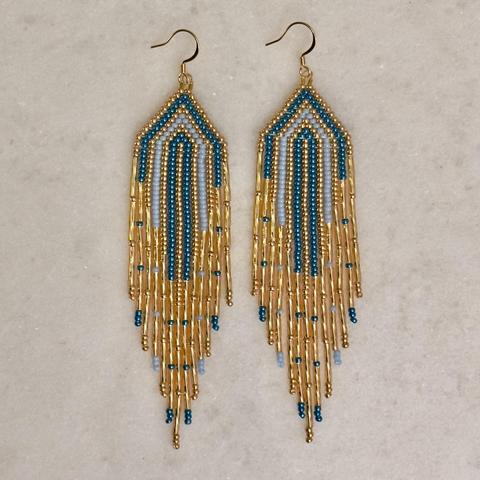 A pair of gold, metallic blue, and light blue beaded fringe earrings on a marble background