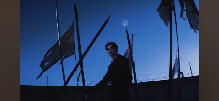 Bang Chan in the Railway video with a blue full moon in the sky behind him