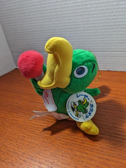 Green bird with a yellow tucan beak, holding a red topped microphone, beak wide open as if singing.