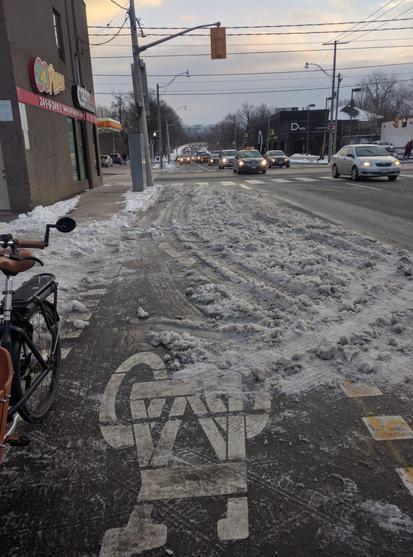 Bicycle lane with bicycle symbol visible underneath snow, covered in tire tracks.