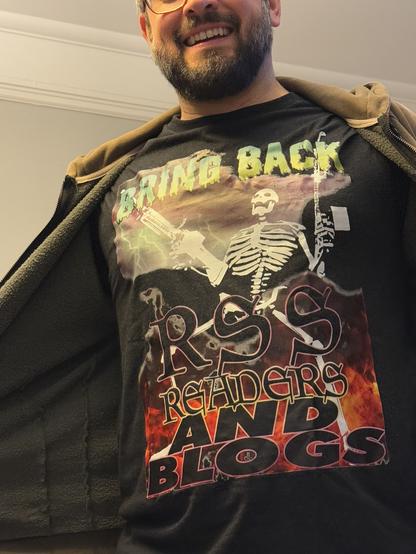 A photo of me in a DASHAREZONE shirt with a skeleton on it holding gigantic guns that says “BRING BACK RSS READERS AND BLOGS”