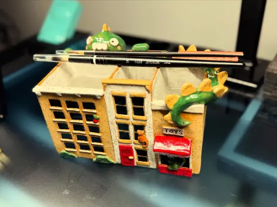 Various angles of a ceramic water container with three partitions having a facade of three buildings with a large Zilla like character peeking up over top from the back, while his tail wraps up and over the right hand side.