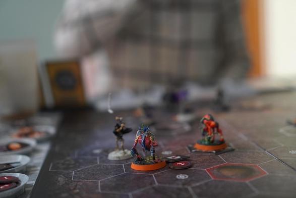 Minatures on a hexagonal grid, a skeleton is standing next to a demon bird type figure. Lots of tokens off to the side.