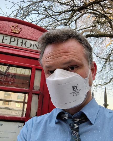 Man wearing FFP3 respirator mask in front of a red UK phone box.