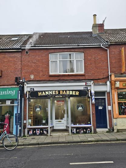 Photo of the shop front of 'Hannes Barder'. White door and dark blue frame with gold, heavy, curved  serif allcaps lettering.