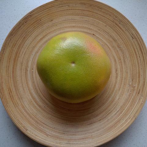 eine Pomelo liegt auf einer hölzernen Schüssel
