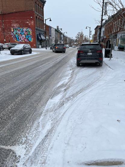 An image of a street in a small town, everything covered with a dusting of snow. A few people are walking while wearing appropriate snow gear.