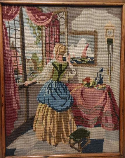 A picture of a woman standing at a window, facing away from the viewer. She is wearing a white, green, blue and yellow outfit; the curtains around the window are pink, as is the drape on the table behind her. On the wall behind the table is a painting of sailing ships at sea, and a pendulum clock.

The picture is rendered in a style of cross-stitch which makes it effectively made out of largish square pixels, and very few colours of wool are used, so that the folds in the curtains, the tablecloth and the woman's clothes must be conveyed using only two or three shades of each main colour.