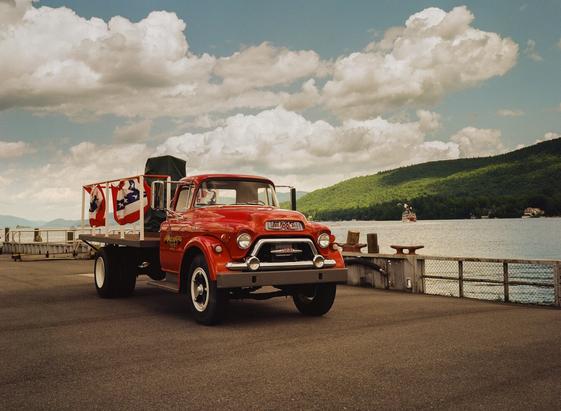 A red, vintage GMC truck with American flag bunting on a dock overlooking Lake George at the Lake George docks.