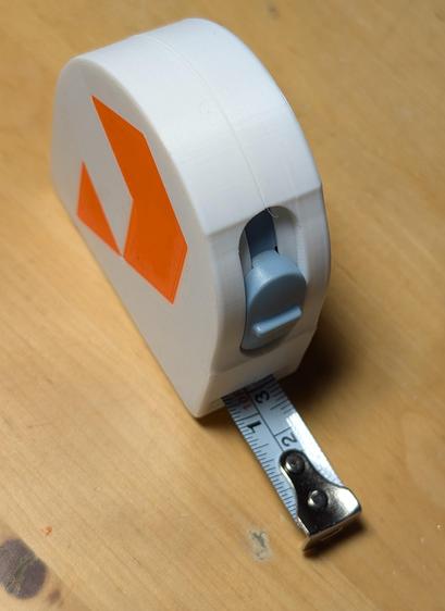 A white tape measure with an orange Printables "P" on the side. A wood surface is in the background.