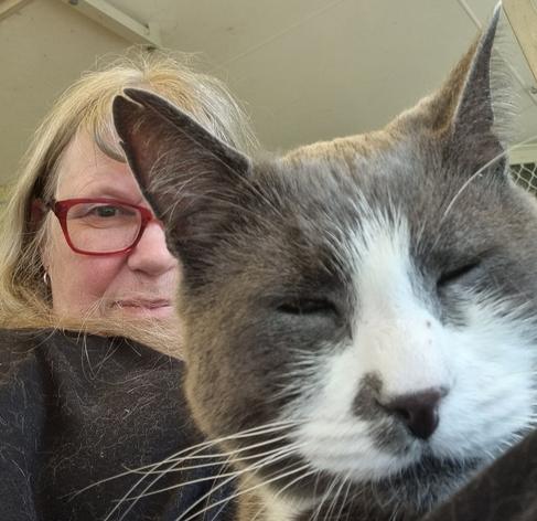 The close-up face of a blue and white cat. His eyes are shut. Half hidden behind him is my face. I'm wearing red-rimmed glasses, no make-up, and my blondish hair is loose.