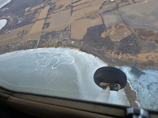 Above view of a design scratched into the ice of a lake near the shore. It is sizeable, looking to be about 10 properties wide. My best guess is that it is an ice track for ice racing but alas it wasn't labelled.