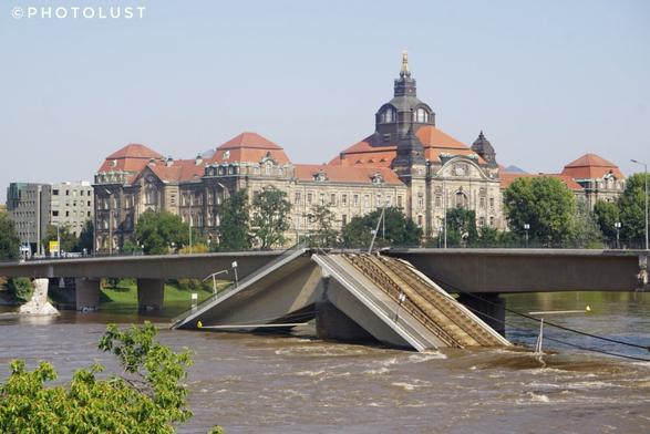 Farbfoto der teilweise eingestürzten Carolabrücke über die Elbe, die gerade Hochwasser führt, in Dresden. Das Gebäude im Hintergrund ist die Sächsische Staatskanzlei.