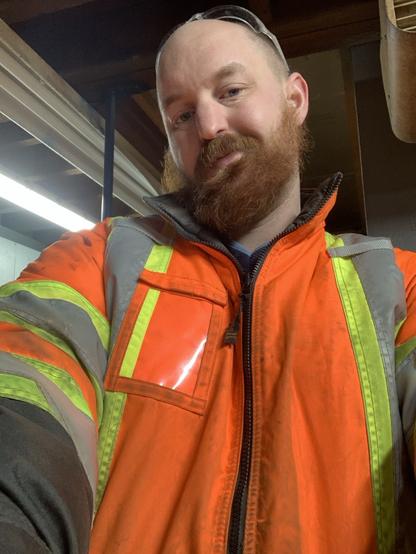 A broad COs male with a big red beard and a reflective jacket offers out a hug. His work enthusiasm level is pretty low