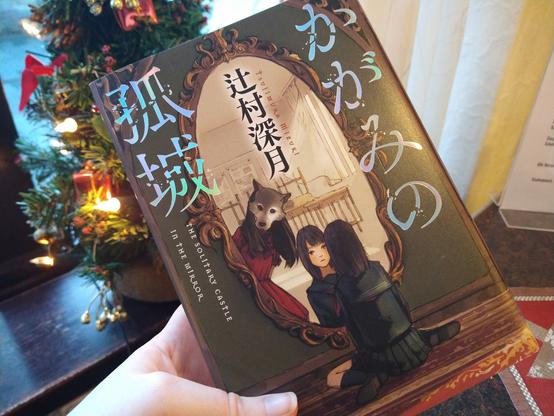 『鏡の孤城』という本の表紙。背景は喫茶店のテーブルやクリスマスの飾り